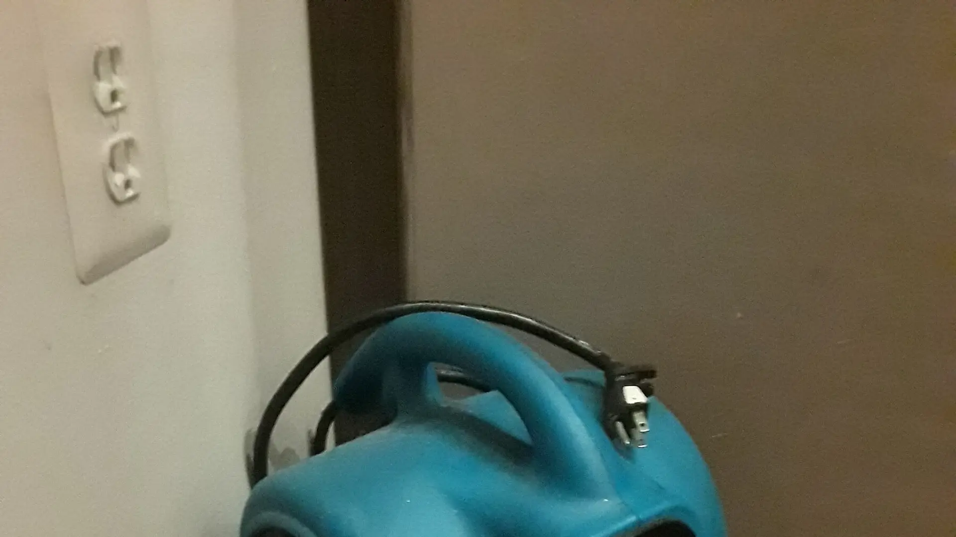 Blue air mover drying a wet floor in the corner of a room